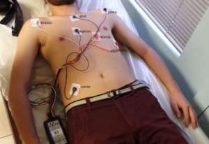Paciente deitado numa maca onde estão sendo colocados os eletrodos de holter no peito e gravador na cintura