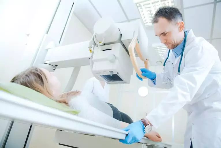 Técnico com posicionando em radiologia de uma paciente deitada na mesa de rx